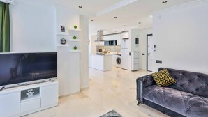 A modern living room with a flat-screen TV, a dark grey sofa with a patterned cushion, and a small white cabinet with a decorative item. - Villa Tanyeli 1 - Three Bedroom Villa, Sleeps 6 (Kalkan)