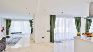 A spacious living room with a large window, a sofa, a coffee table, and a dining area with a bench. - Villa Tanyeli 1 - Three Bedroom Villa, Sleeps 6 (Kalkan)