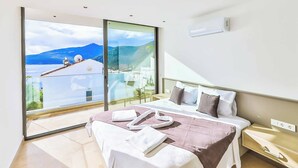 A modern bedroom with a large bed, a bedside table, and a view of a mountainous landscape through a large window. - Villa Marni - Six Bedroom Villa, Sleeps 12 (Kalkan)