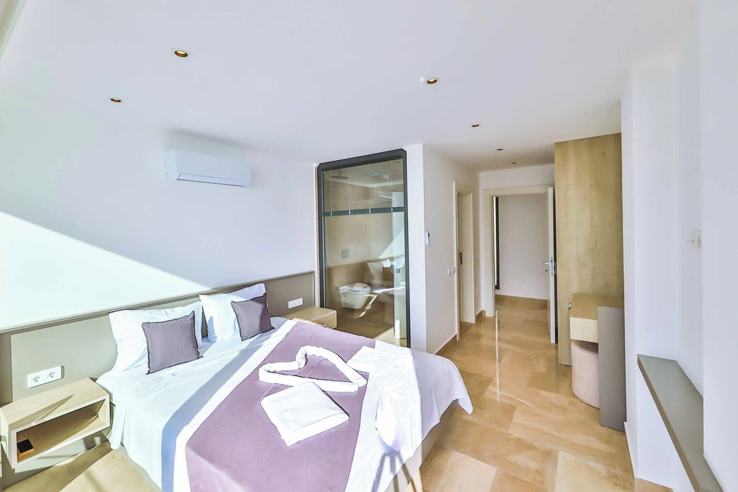A modern hotel room with a bed, bedside table, and a glass-enclosed bathroom.