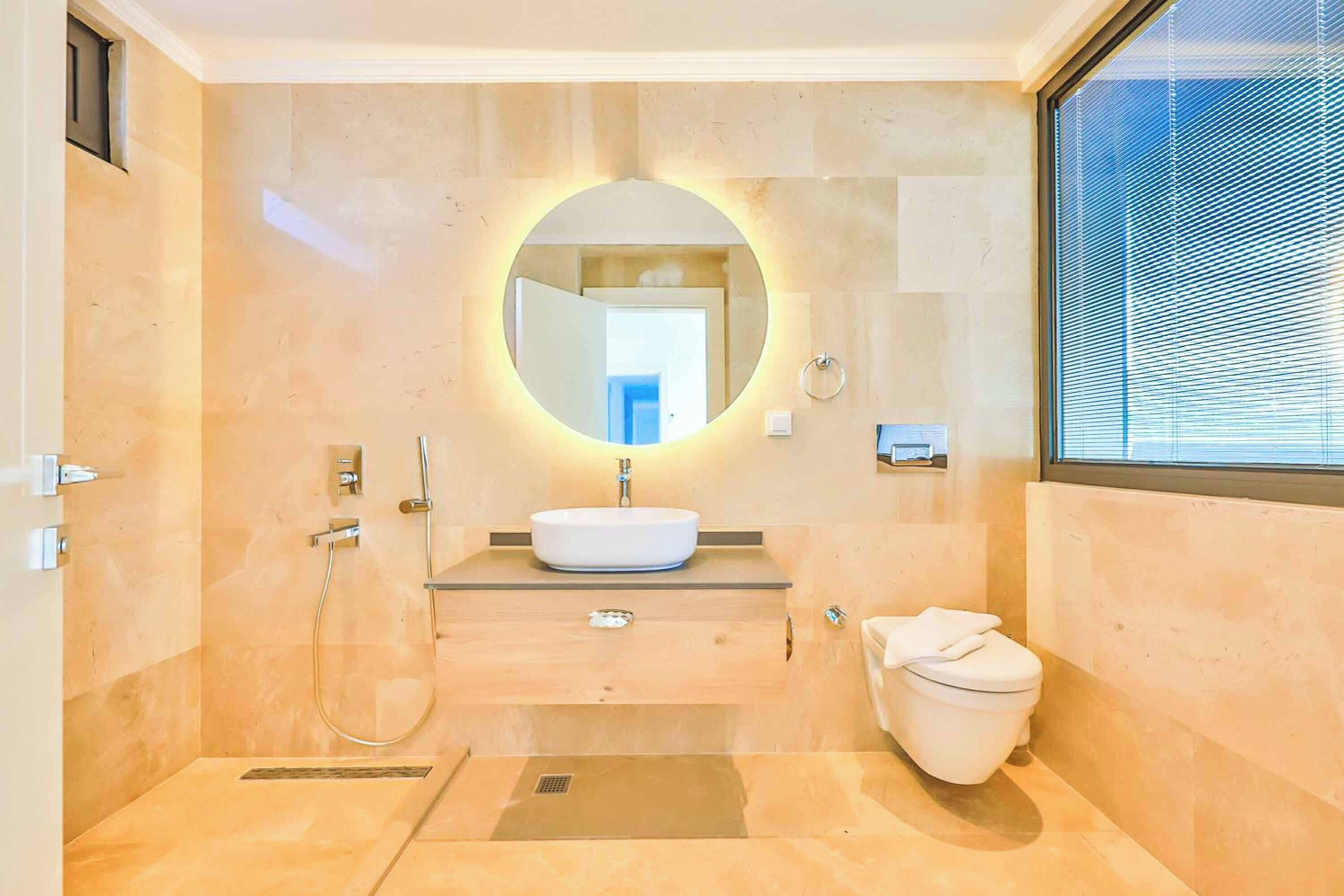 Een moderne badkamer met een ronde spiegel, een wastafel en een toilet.