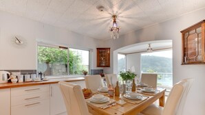 Una cocina moderna con armarios blancos, una mesa de comedor de madera preparada para cuatro comensales y vistas al exterior a través de amplios ventanales.