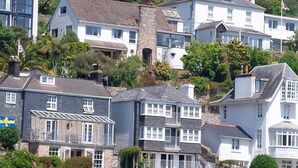 Un pueblo costero con una mezcla de edificios residenciales, incluyendo casas de fachadas de piedra y balcones, y un muelle con una pequeña embarcación.