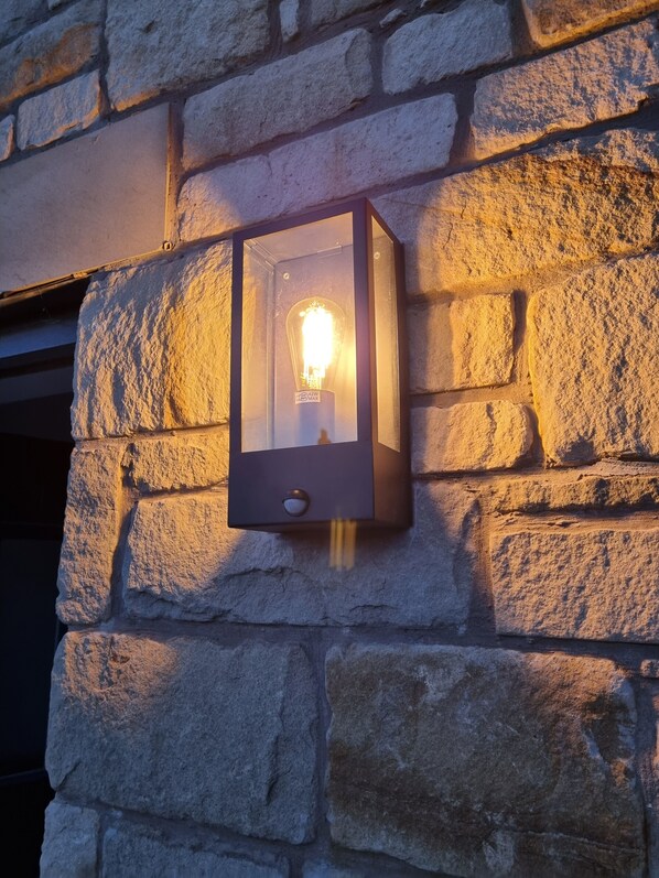 Un luminaire mural fixé au mur, avec une ampoule visible à l’intérieur, placé devant un mur en pierre.