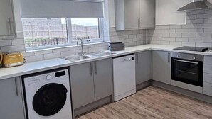 A modern kitchen with grey cabinets, a built-in washing machine, a dishwasher, and a window with a view of a fence. - Comfortable, modern cottage that sleeps up to 6. Ideal hub to explore Northumberland! (Morpeth)