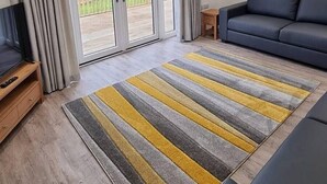 A modern living room with a sofa, a TV, and a large sliding glass door leading to a balcony. - Comfortable, modern cottage that sleeps up to 6. Ideal hub to explore Northumberland! (Morpeth)