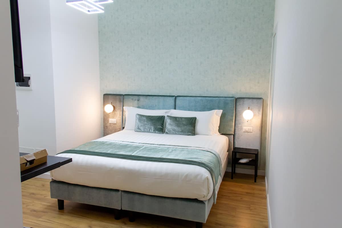 A neatly made bed with a green headboard, two bedside lamps, and a small nightstand.