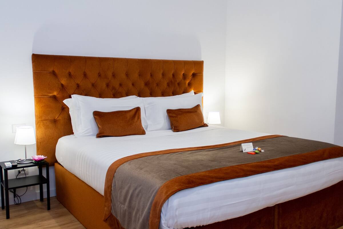 A neatly made bed with a tufted headboard, white linens, and brown pillows.