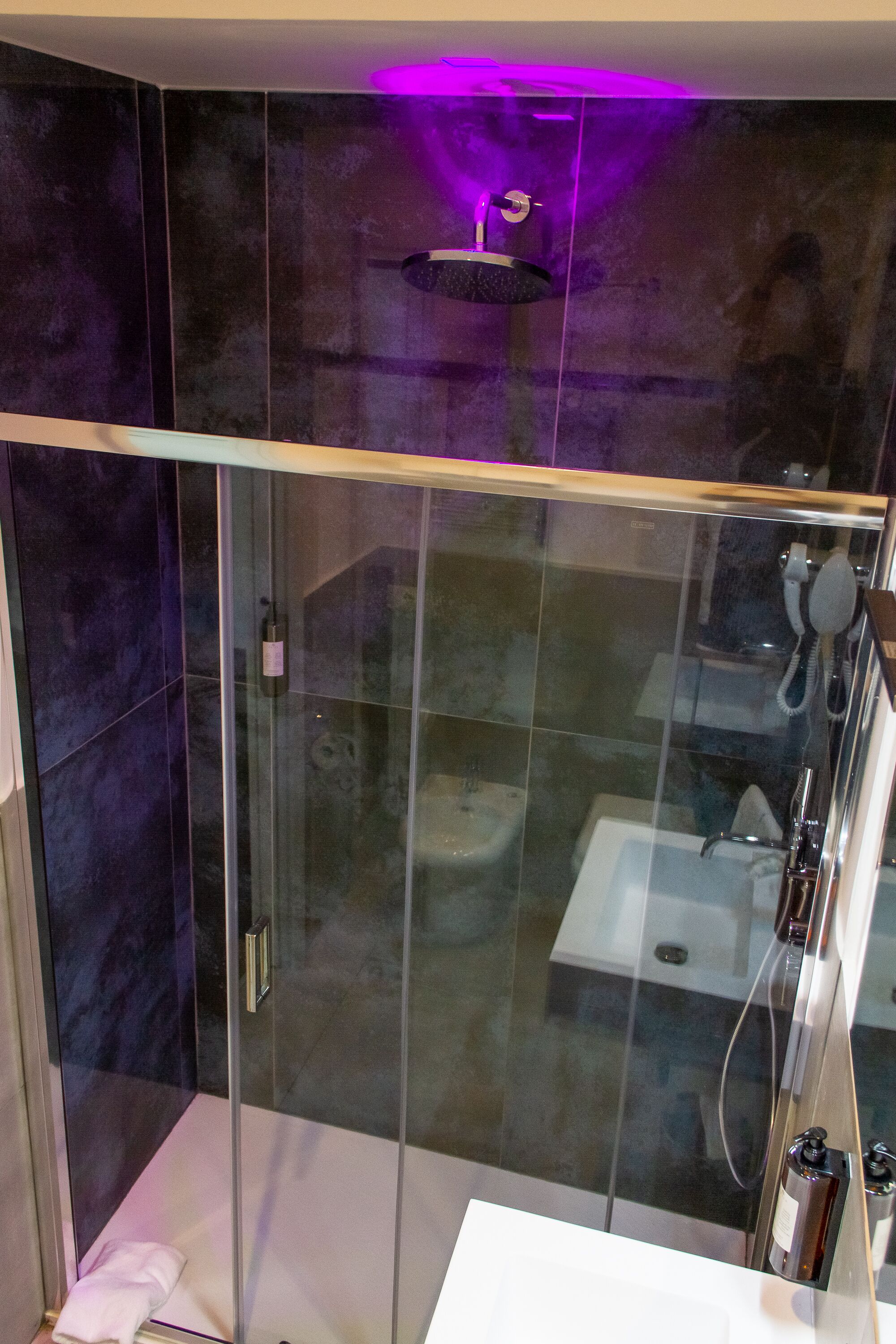 Un baño moderno con cabina de ducha de vidrio, un lavabo blanco y pared revestida de mármol.