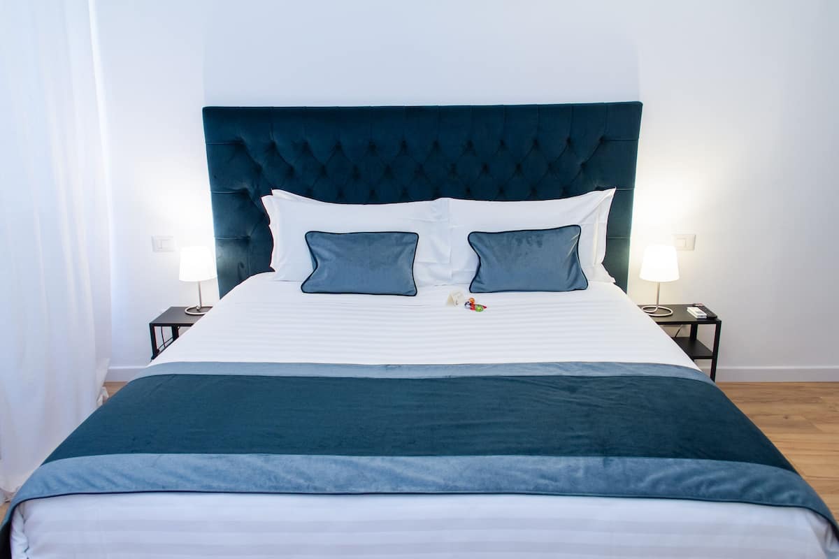 A neatly made bed with a dark headboard, white and blue bedding, and two bedside lamps.