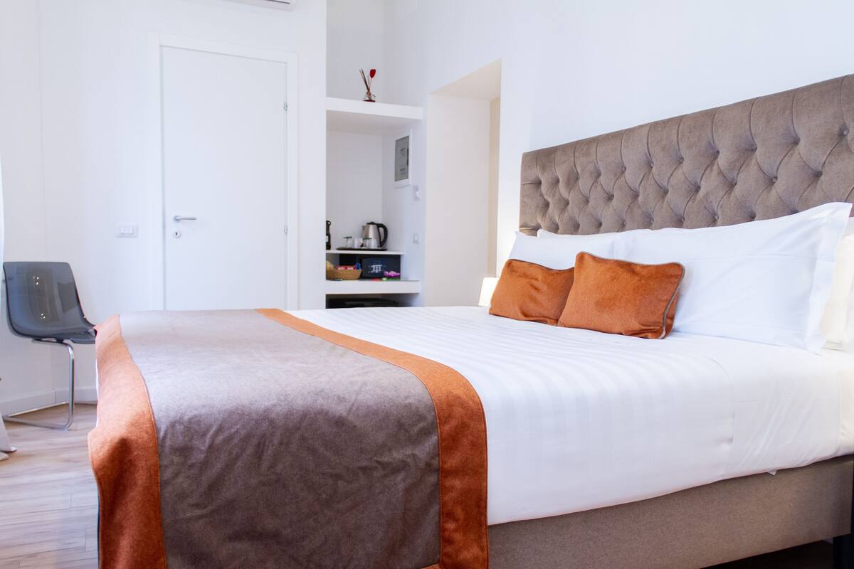 A neatly made bed with a grey headboard, white bedding, and orange accents.