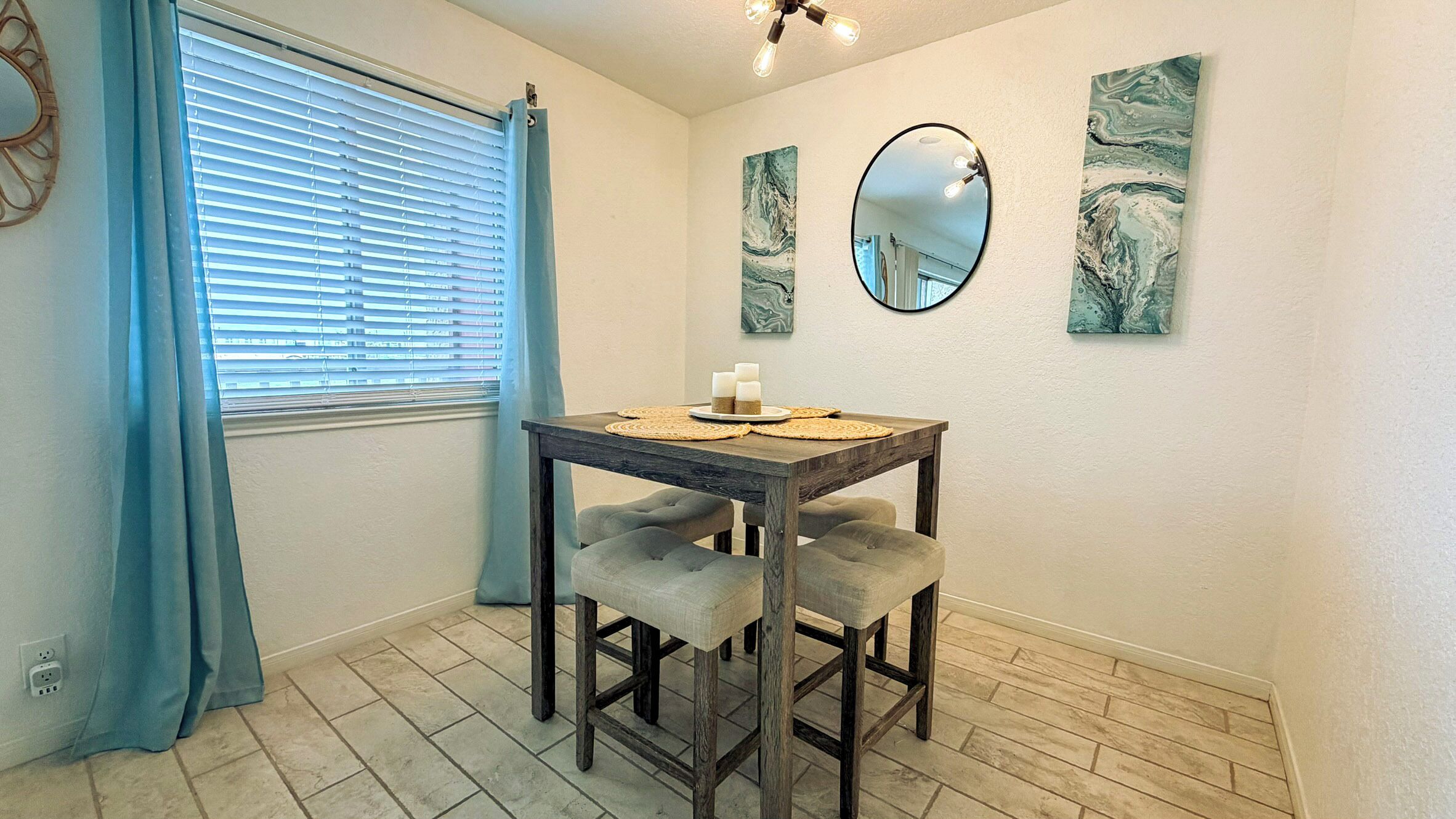 Een eetgedeelte met een houten tafel, twee comfortabele stoelen, een spiegel en kunstwerken aan de muur.