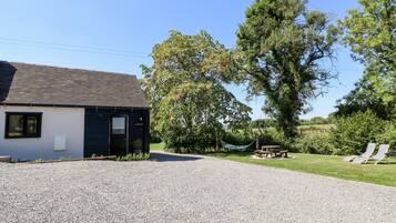 A building with a gravel driveway, a picnic table, and two striped lounge chairs.