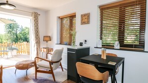 Un comedor moderno con mesa y sillas, una pequeña cocina y ventanas grandes con persianas.