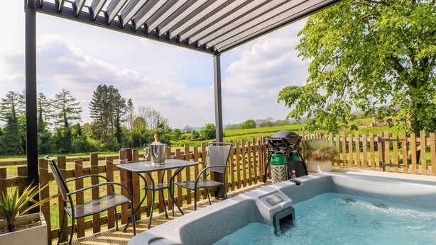 Un jacuzzi bajo una pérgola con vistas a una valla de madera y follaje.