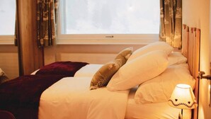 Una habitación de hotel con cama, ventana con cortinas, lámpara y vistas a árboles.