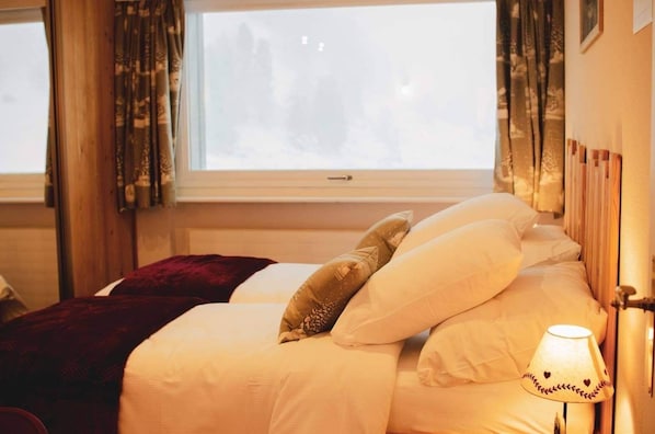 Ein Hotelzimmer mit Bett, einem Vorhangfenster, einer Lampe und Blick auf Bäume.