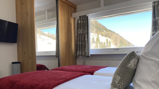 Un dormitorio con dos camas, techo de madera, ventana con vista a la montaña y un altavoz.