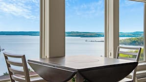 A table and chairs by a large window with a view of a lake and distant hills. - Happy Place Condo - Stunning Table Rock Lake Views (Branson)