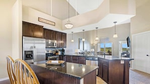 A spacious kitchen with dark wood cabinets, stainless steel appliances, and a large island with seating. - Happy Place Condo - Stunning Table Rock Lake Views (Branson)