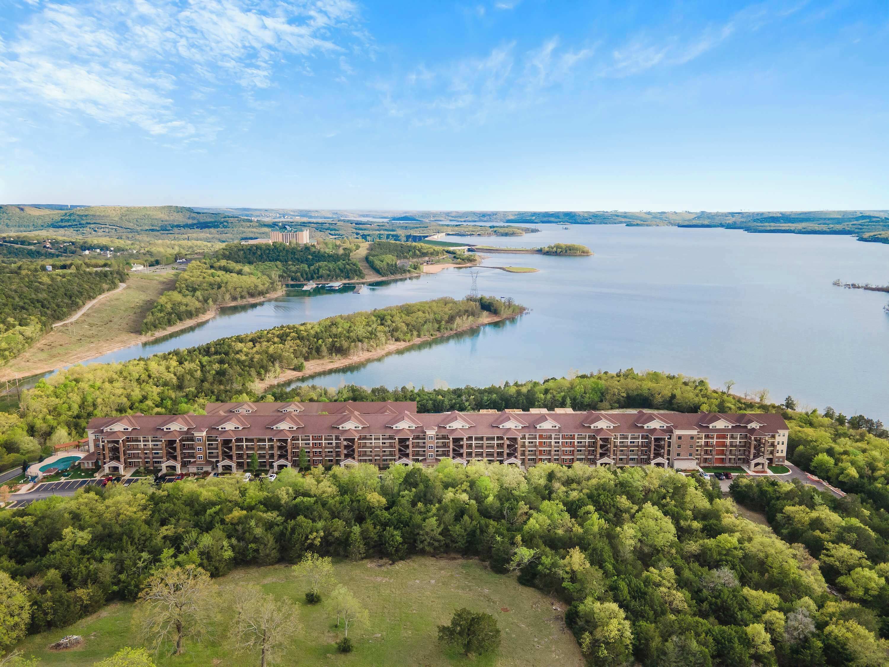 Un hôtel à plusieurs étages doté d’une cour intérieure, entouré d’une végétation luxuriante et bordé d’une vaste étendue d’eau.