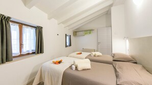 Ein Hotelzimmer mit zwei Betten, einem Fenster mit Vorhängen, einem Spiegel und einem Regal mit Handtüchern.