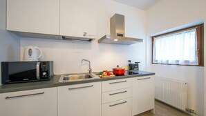 Eine moderne Küche mit weißen Schränken, einer Edelstahl-Spüle, einer Mikrowelle und einem roten Topf auf der Arbeitsfläche.