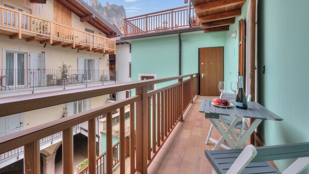 Ein Balkon mit Holzwerteln, ein Tisch mit Flasche und Gläsern und ein Blick auf einen Berg im Hintergrund.
