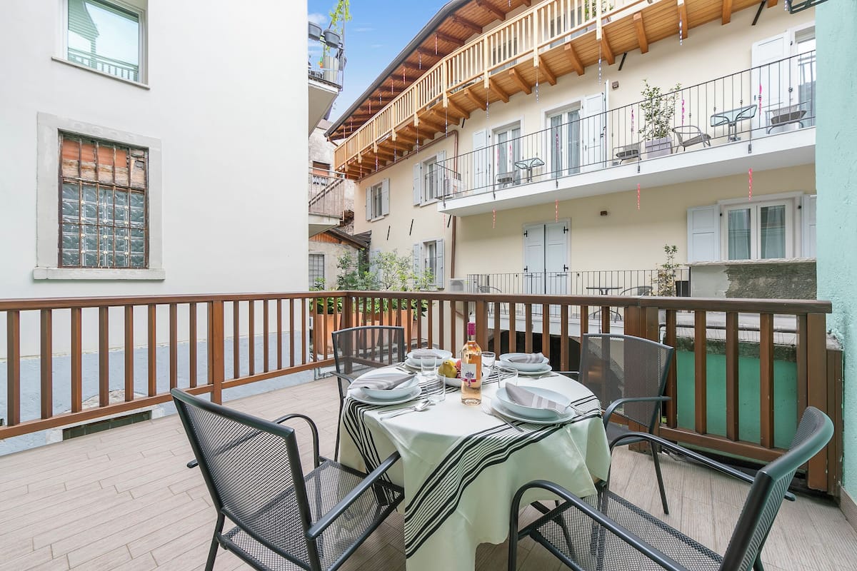 A balcony with a table set for dining, surrounded by metal chairs.