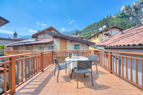 A terrace with a table and chairs, a wooden railing, and a mountainous backdrop.
