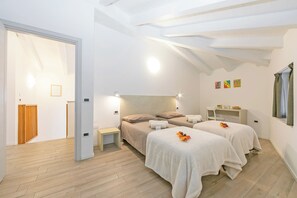 A bedroom with two beds, a bedside table, a nightstand, a desk, and a window.