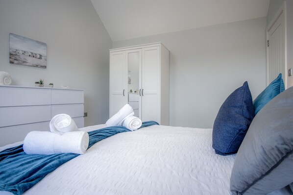 A neatly made bed with rolled white towels, a blue blanket, and two pillows.