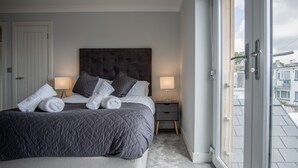 A bedroom with a large bed, two bedside tables with lamps, a door, and a view through a glass door.