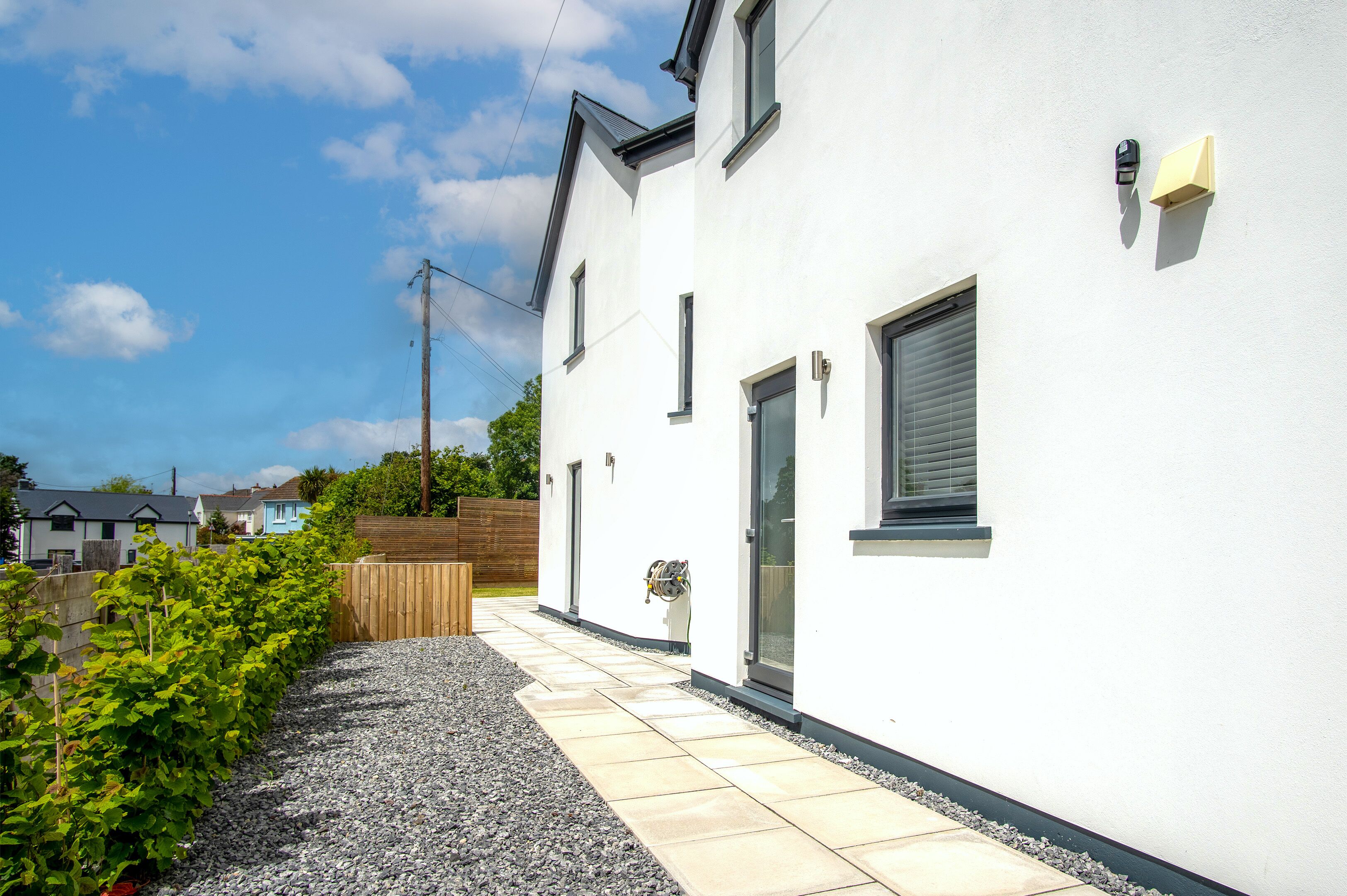 A modern house with a white exterior, a gravel pathway, and a wooden fence.