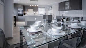 A modern kitchen with dark cabinets, a central island, and a dining area with a glass table set for six.