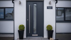 A modern building with a dark grey door, two potted plants, and a sign reading "Gower View".