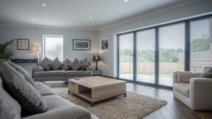 A modern living room with a grey sofa, a wooden coffee table, and a large window with blinds.