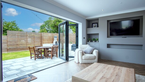 A modern living room with a large TV, a sofa, a coffee table, and a sliding glass door leading to an outdoor patio with a barbecue.