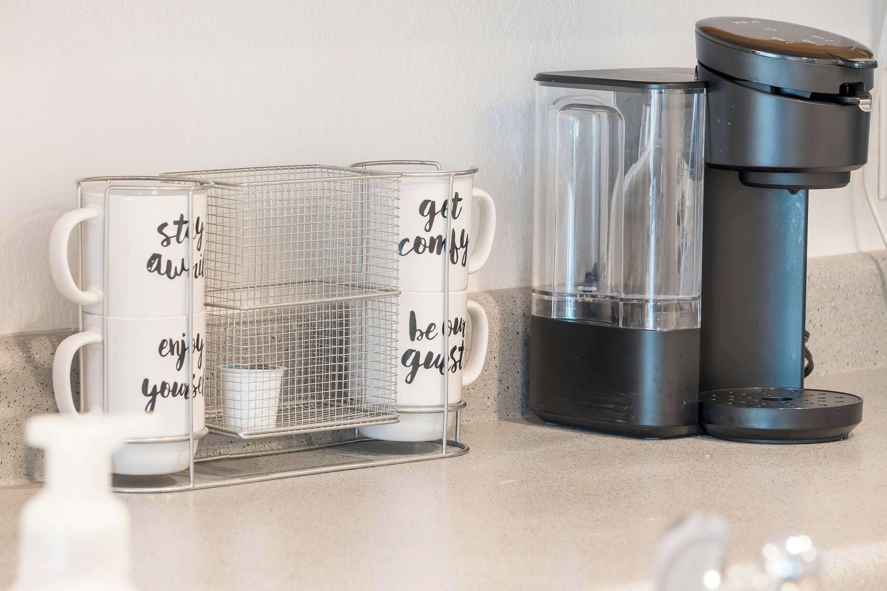 A kitchen counter with a coffee maker, a water dispenser, and three mugs with motivational phrases.