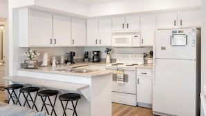 A modern kitchen with white cabinets, a central island with stools, a microwave, stove, and refrigerator. - Boatin & Floatin on Table Rock Lake in the Ozarks! (Kimberling City)