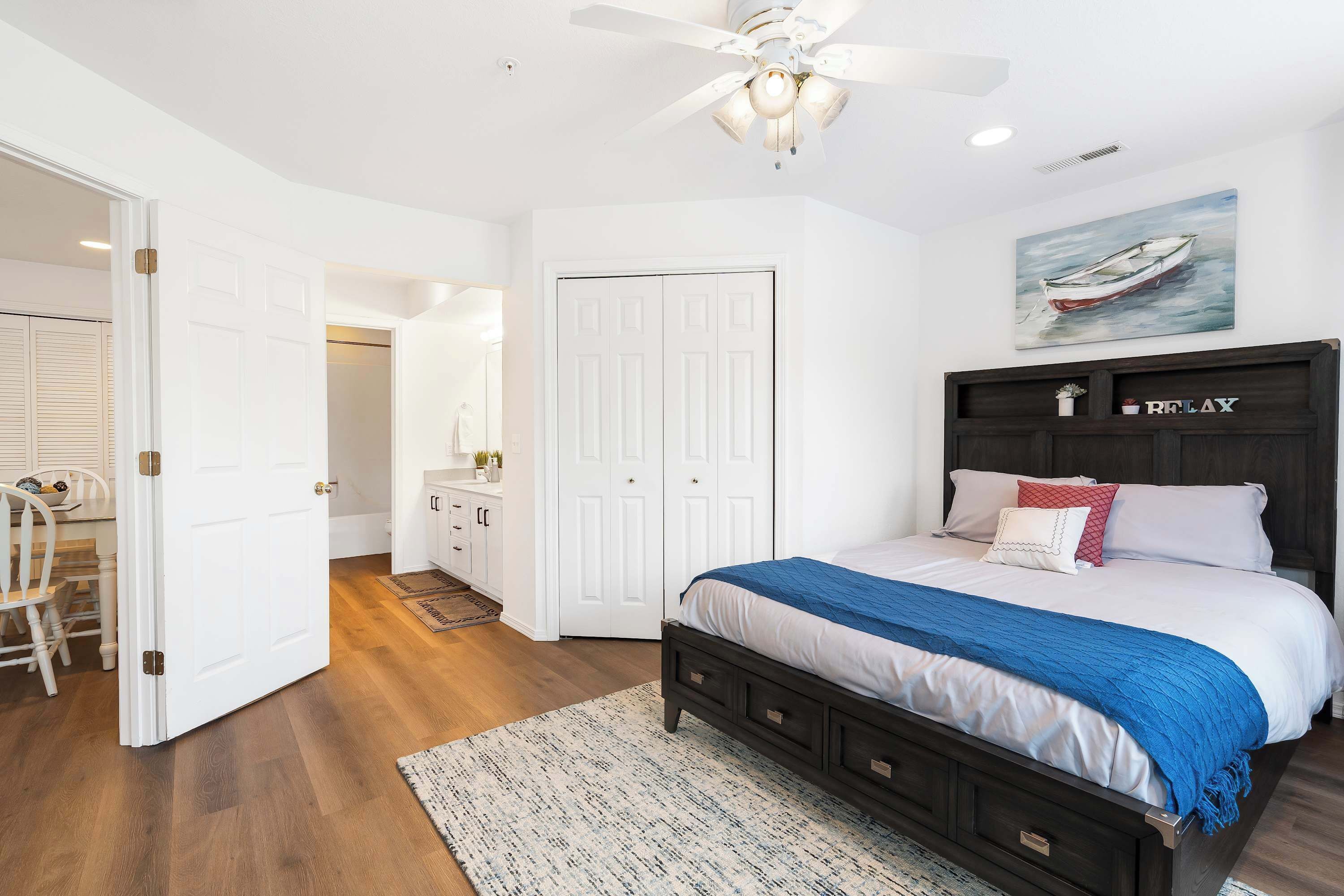 A bedroom with a bed, a ceiling fan, a painting, and a wardrobe.