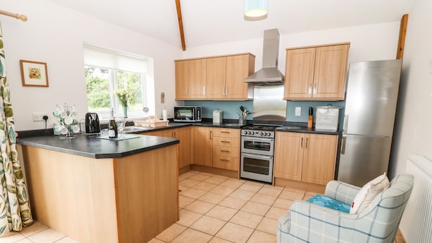 A kitchen with wooden cabinets, a built-in oven, a microwave, and a refrigerator. - Dinas Farmhouse Annex (Caernarfon)