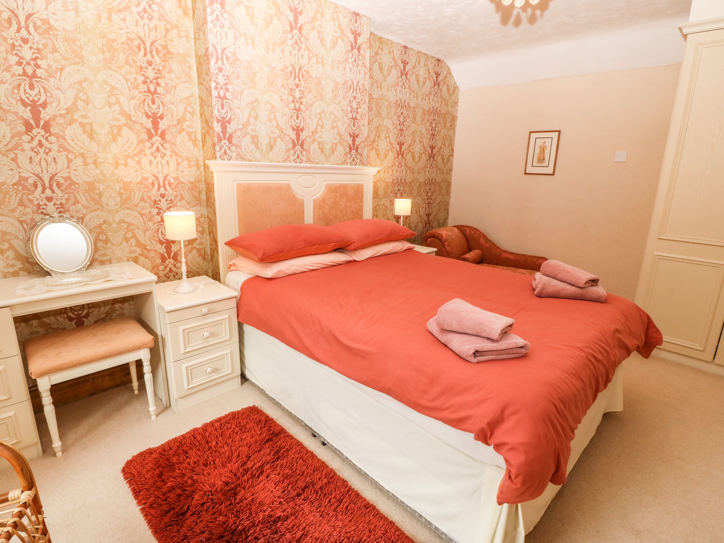 A neatly arranged bedroom with a large bed, a bedside table with a lamp, a chair, and a small bench.