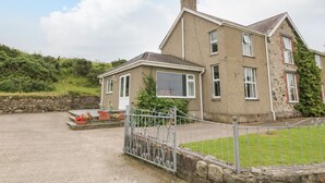 A two-story house with a stone facade, a large window, and a metal gate in front. - Dinas Farmhouse Annex (Caernarfon)