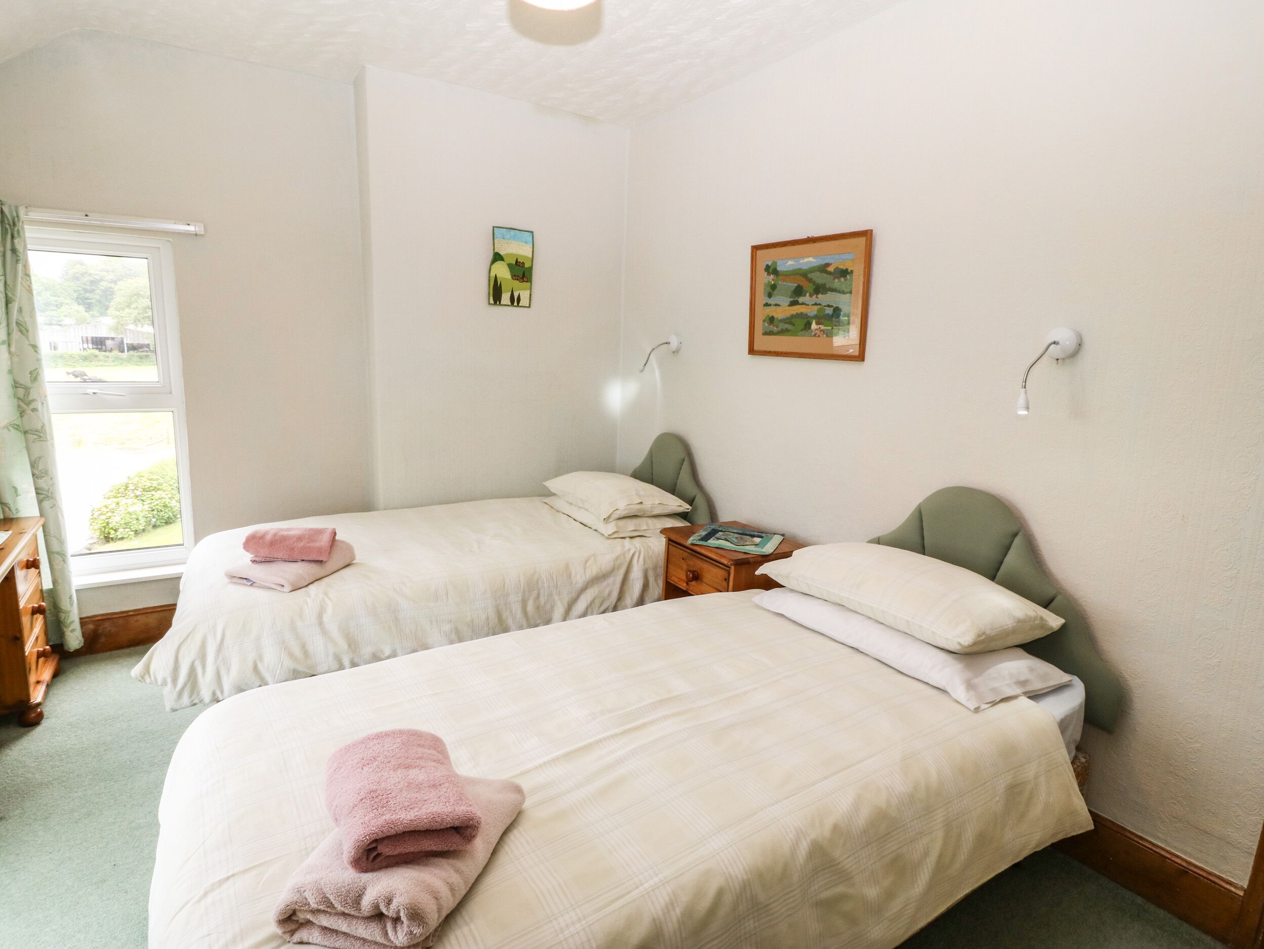 Een kamer met twee enkele bedden, een nachtkastje, een lamp en een raam met gordijnen.