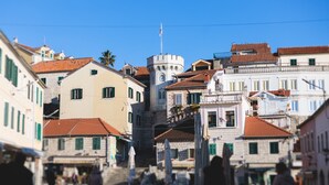 A narrow street with historic buildings, a prominent tower, and a clear blue sky. - Pool Villa Luxoria Trebesin (Herceg Novi)