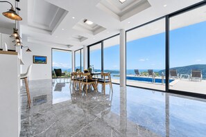 A spacious room with a large dining table, chairs, and a view of a pool and mountains. - Pool Villa Luxoria Trebesin (Herceg Novi)