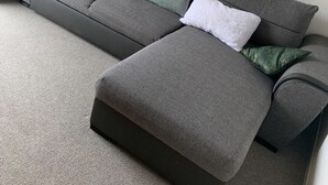 Ein graues Ecksofa mit vielen Kissen in einem Raum mit geneigter Decke und einem gerahmten Gemälde an der Wand.
