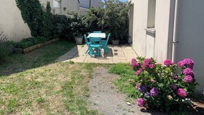 Ein kleiner Innenhof mit Tisch und Stühlen, umgeben von einem Garten mit blühenden Pflanzen.
