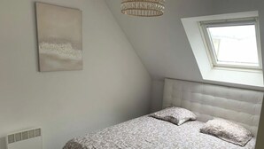 Ein Schlafzimmer mit geneigter Decke, einem Bett mit gemustertem Überwurf, einem weißen Kopfteil, einer Deckenleuchte und einem Fenster mit Blick.